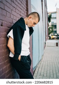 Candid Waist Portrait Of A Trendy Handsome Young Man In City. Caucasian In Early 20s Man Stands Near Wall In Urban Setup. Looking Away From Camera. Casually Dressed. Lifestyle Millenials. Short Hair