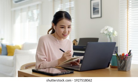 Candid young attractive asian female employee wear earphone listen to digital online course development program in quarantine social distance at home reskill upskill school class for career path. - Shutterstock ID 1927518062