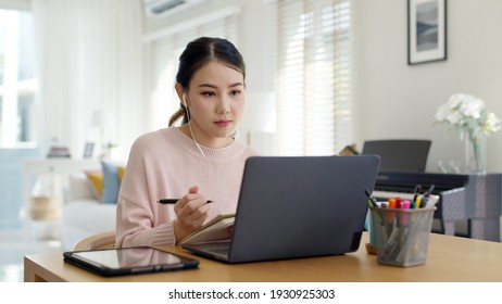 Candid young attractive asian female employee wear earphone listen to digital online course development program in quarantine social distance at home reskill upskill school class for career path. - Shutterstock ID 1930925303