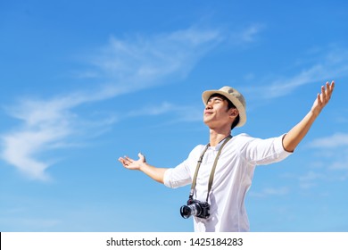 Candid Of Young Attractive Asian Man Close Eyes, Deep Breath And Wide Open Arms In Blue Sky View Background Feeling Wind And Sunshine. Happy Asian Hipster Male In Youth Freedom Culture Travel Concept.