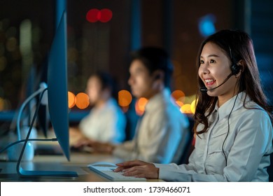 Candid of young happy asian woman call centre sitting in office at night shift overtime in concept telesale, teleservice, telemarketing, coronavirus information center, bank or airline representative - Powered by Shutterstock