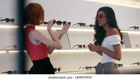 Candid young multiracial women shopping for sunglasses. Pretty girls trying on sunwear at store