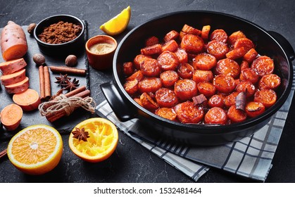 candied yams, sweet potatoes cooked with cinnamon, brown sugar and butter in a black ceramic dish. ingredients on a stone board on a concrete table,  horizontal view from above