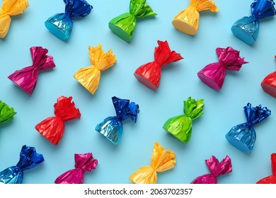 Candies in colorful wrappers on light blue background, flat lay