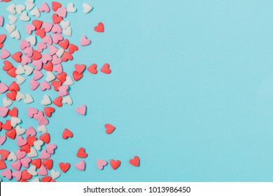 Candies hearts of pastel colors on blue paper. Flat lay.