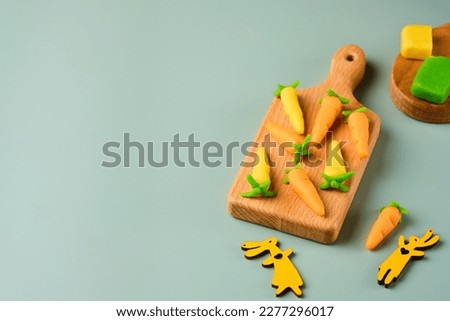 Candies, marzipan carrots handmade from colored marzipan on a wooden mini board on a plain green vinyl background. Sweets, edible decor for cakes