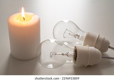 Candle with burning flame, next to unlit bulbs. Energy saving and rationing. Increase in tariffs and energy crisis.
 - Shutterstock ID 2196915859