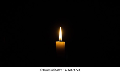 A Candle Burns In The Darkness, Copy Space. A Lit White Candle On A Black Background. Symbol Of Eternal Memory, Mourning, Minutes Of Silence, Memorial Day. The Concept Of Loss And To The Memory.