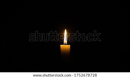 A candle burns in the darkness, copy space. A lit white candle on a black background. Symbol of eternal memory, mourning, minutes of silence, memorial day. The concept of loss and to the memory.