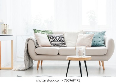 Candle In A Glass Jar On Table In Front Of Beige Sofa With Pillows In Scandinavian Style Living Room