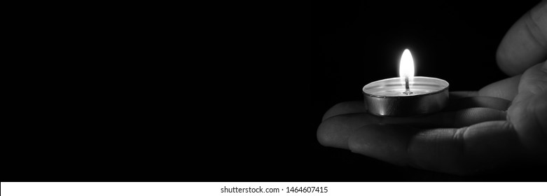 Candle in hand burning in the black background. Copy space. Black and white photo. The concept of mourn, grief or mourning.