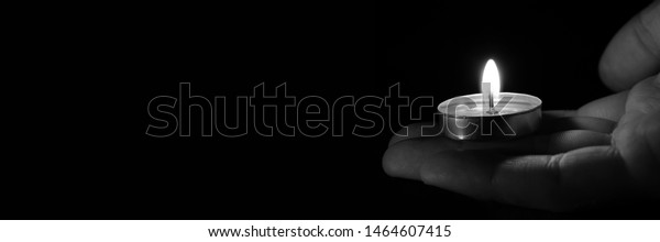 Candle in hand burning in the black background.
Copy space. Black and white photo. The concept of mourn, grief or
mourning.