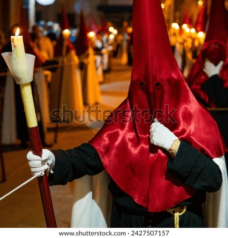 Candle held by unrecognized Member of a brotherhood dressed in tunic and red capirucho in an Holy Week procession at night. Devotee, copy space, nazarene