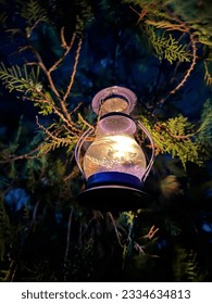 A candle lantern hanging in a pine tree.