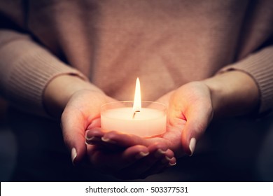 Candle light glowing in woman's hands. Praying, faith, religion concept.