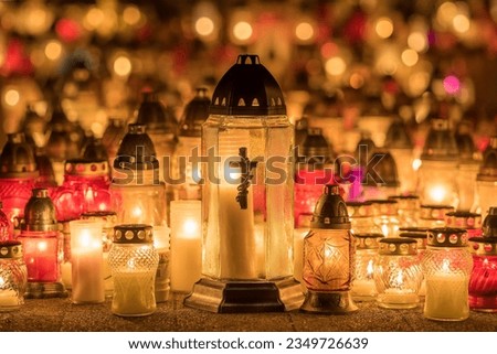 Candle lights on graves and tombstones at a cemetery in Poland during All Saints Day, Zaduszki day, and Day of the Dead. Lit candles illuminate the graves at a Christian cemetery at night.