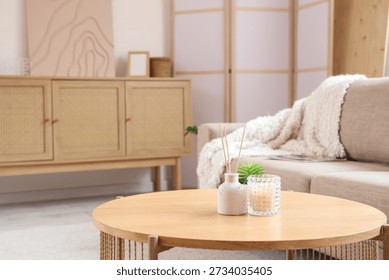 Candle and reed diffuser on table in interior of living room, closeup