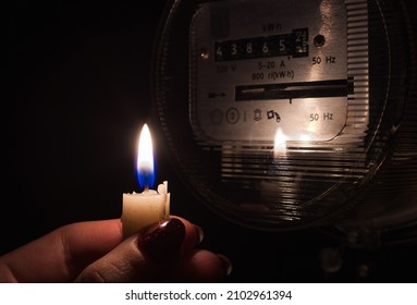 Candle shining light in the dark near electricity meter during power outage at home. Blackout city, no electricity symbolic image.