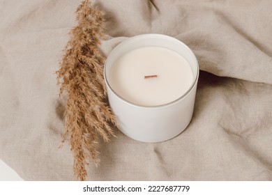 Candle in white glass jar with pampas grass on linen towel. Candle with wooden wick. Home decoration, minimal interior, Scandinavian style