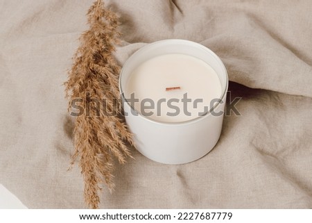 Candle in white glass jar with pampas grass on linen towel. Candle with wooden wick. Home decoration, minimal interior, Scandinavian style