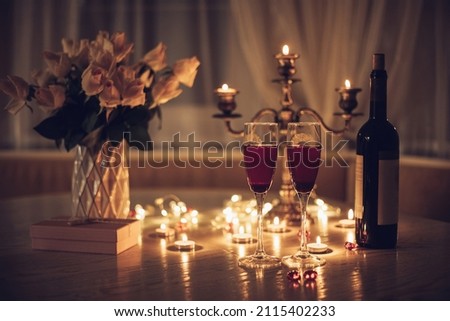 Candlelight date. Glasses with wine candles bouquet of rose and gift box on table. Romantic candlelight dinner at home at night