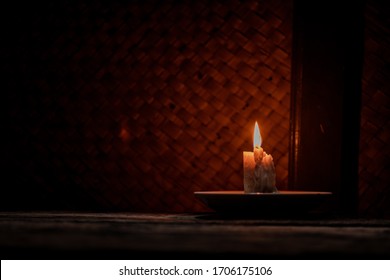 Candlelight illuminates the dark room of a rural house where there is a rustic wooden table. Concept of rural areas that lack access to electricity for lighting.