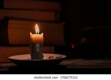 Candlelight illuminates the dark room of a rural house where there is the books on a rustic wooden table. Concept of education in rural areas that lack access to electricity for lighting.
