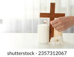 Candles, cross and hand on light background, space for text