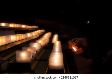 candles in a row with a hand lighting them inside a church during prayer
