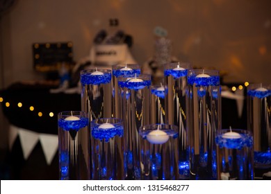 Candles In Water In Tall Glass Containers With Blue Decorations Ready To Be Lighted For A Bar Mitzvah Celebration With The Birthday Cake Blurred In The Background