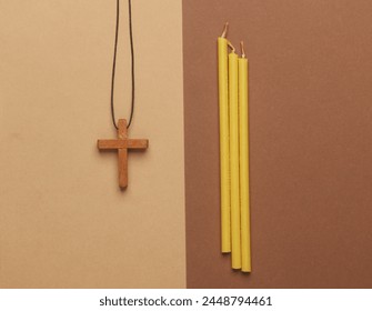 Candles and wooden Christian cross on a string, beige background. Religion, prayer, going to church concept. Top view. Flat l;ay