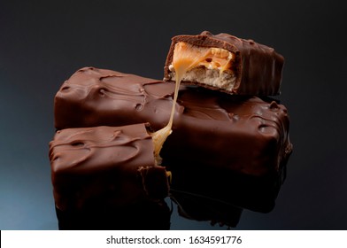 Candy bar, fattening high calorie sweets and junk food concept with generic caramel, nugget and biscuit chocolate bar breaking isolated on dark background