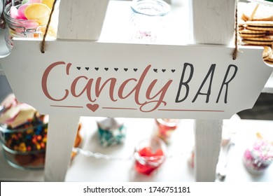 Candy bar lettering on white stand. Various sweets and gummy candies in background. Celebration, party, birthday or wedding concept.
