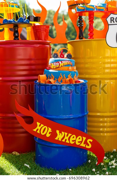 Candy bar on boy\'s birthday party with a lot of\
different candies, popcorn, beverages and big cake standing on a\
barrel. Decorated in bright colors. Hot wheels, cars or racing\
theme. Summer, outdoor