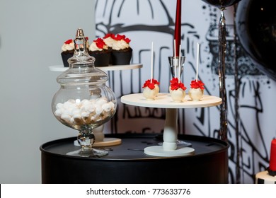 Candy Bar On Woman's Birthday Party With A Lot Of Different Candies, Cupcakes And Big Cake, Standing On Barrels In Black,red, White Colors. Paris Theme, Indoor