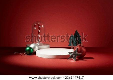 A candy cane inside a glass cage displayed with few sparkling baubles, a star and christmas trees. Blank space on the white podium to show your product