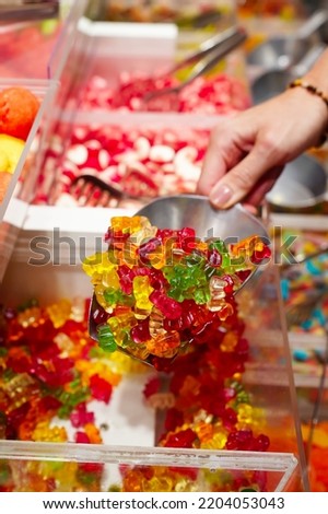 candy store. Woman hand with scoop taking colorful delicious candies on counter of shop, grocery, market, cafe. Many colorful candies on grocery stand Dessert, sale, sweet food.