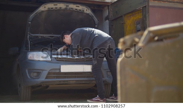 Canister stands in front of young man repairs car\
in garage