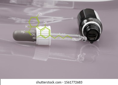 Cannabidiol oil in brown glass bottle, CBD dropper and green structural formular of cannabidiol on dusky pink background
