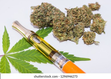 Cannabinoid oil vape pen up close with weed leaf & marijuana buds on white background.