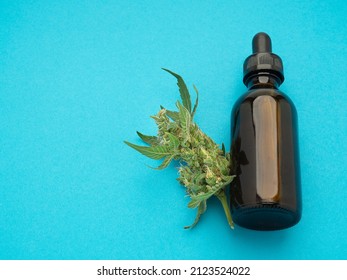 Cannabis CBD Oil Bottle And Marijuana Buds Flower Over A Blue Background. Cannabis Can Help Manage Chronic Pain, Nausea, And Vomiting Resulting From Chemotherapy Treatment