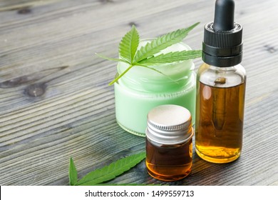 Cannabis CBD Oils In Glass Bottle And CBD Lotion Gel Little Jars With Hemp Leafs On Wooden Table
