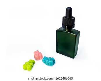 Cannabis extract oil, known as CBD, in a green tincture bottle next to some CBD gummies on a white background