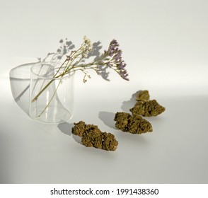 Flores de cannabis yacen junto a flores secas moradas y blancas dentro de un pasto. 