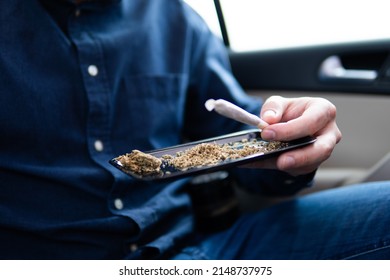 Cannabis Joint Packet Of Weed On A Car Background Close Up Marijuana Joint In Hand Bud Flowers Of Cannabis. Grinder And Shredded