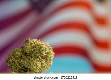 Cannabis Marijuana Flower Nugget On A Table In Front Of A Waving American Flag.