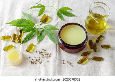 Cannabis medical healing salve, CBD capsules from sativa seeds, hemp oil bottle. Composition with cannabis leaves on fabric of hemp plants. Concept for treatment and relaxation or food supplements