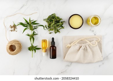 Cannabis products. Cannabis medical healing balm salve, CBD and food oil bottles, tea leaves, sativa seeds, hemp rope and fabric bag. Top view composition with hemp plant on marble background - Shutterstock ID 2058324410