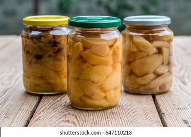 Canned apple and pear compotes, preserve in large glass jars outdoors on rustic wooden table
