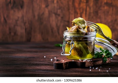 Canned artichokes in olive oil, in glass jar, rustic wooden kitchen table background, still life, sfallow DOF selective focus
